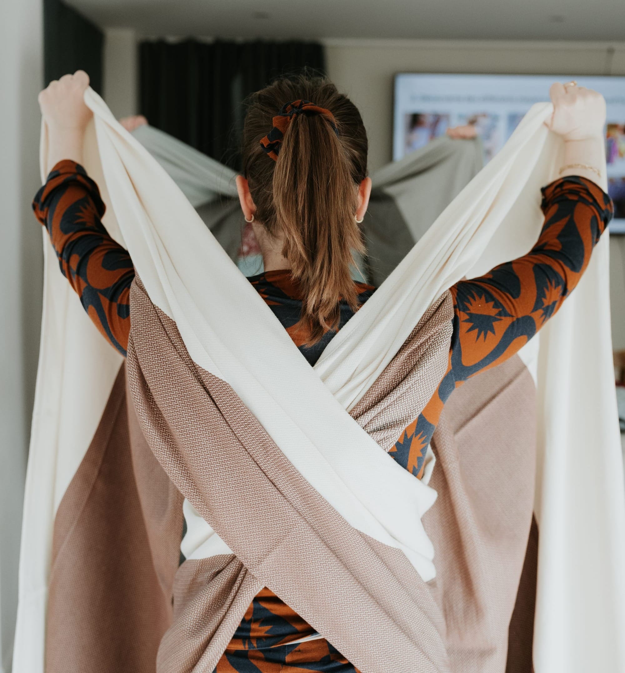 Instructrice de portage montrant un nouage d’écharpe physiologique lors d’un atelier, vue de dos.