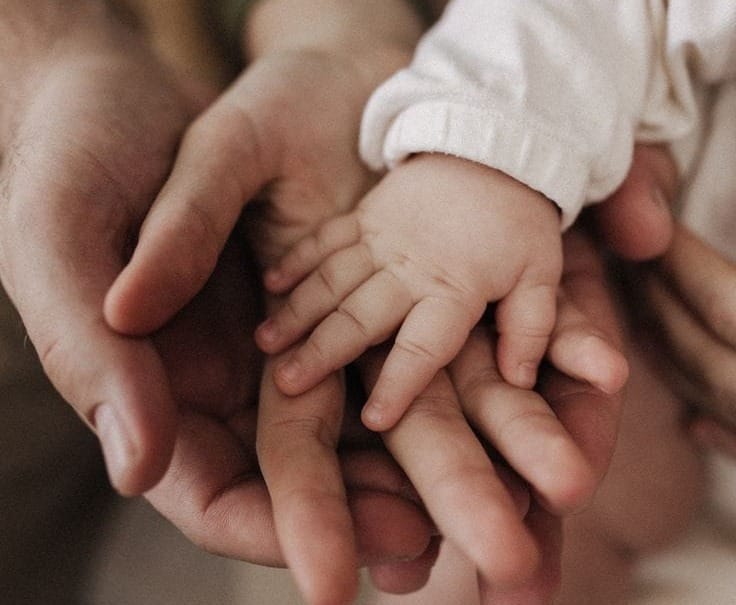 Main d’un parent tenant délicatement la main de son nouveau-né, symbole de lien d’attachement, de sécurité et de proximité parent-bébé.