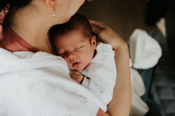 Bébé endormi paisiblement dans les bras de sa mère, illustrant le sommeil réparateur et la sérénité parentale">
