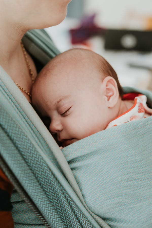 Bébé endormi contre le torse de son parent dans une écharpe de portage physiologique, symbole de douceur et de lien parent-bébé.