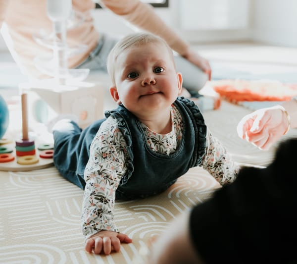 Bébé allongé sur le ventre pendant un atelier d’éveil moteur, observant son environnement, sous le regard bienveillant d’un parent.