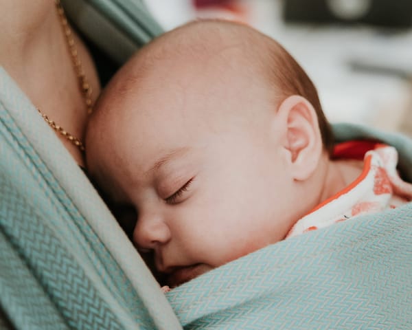 Bébé endormi contre le torse de son parent dans une écharpe de portage physiologique, symbole de douceur et de lien parent-bébé.