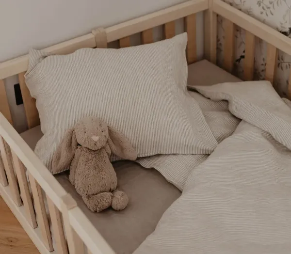 Lit de bébé dans une chambre douce et apaisante, avec matelas, linge de lit et peluche, illustrant un environnement sécurisé et propice au sommeil du bébé.
